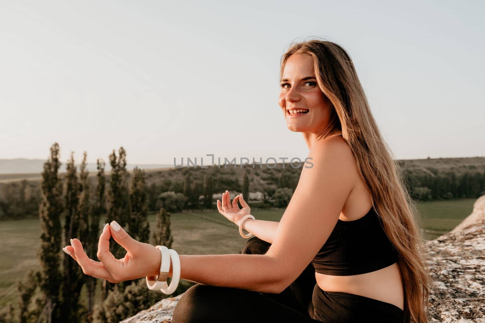 Fitness woman. Well looking middle aged woman with long hair, fitness instructor in leggings and tops doing stretching and pilates on the rock near forest. Female fitness yoga routine concept. by panophotograph