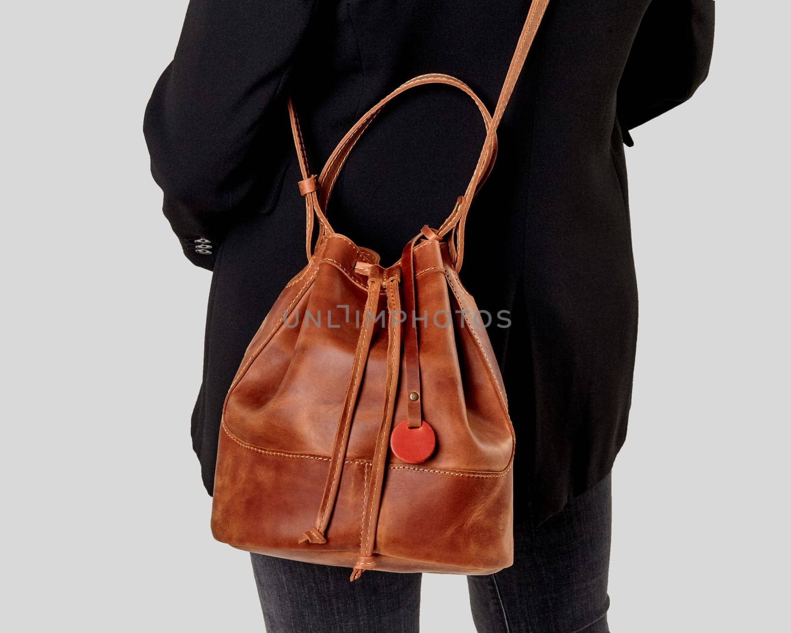 Woman in black coat carrying chic tan leather bucket bag with motivational tagline over shoulder. Stylish artisanal women accessories