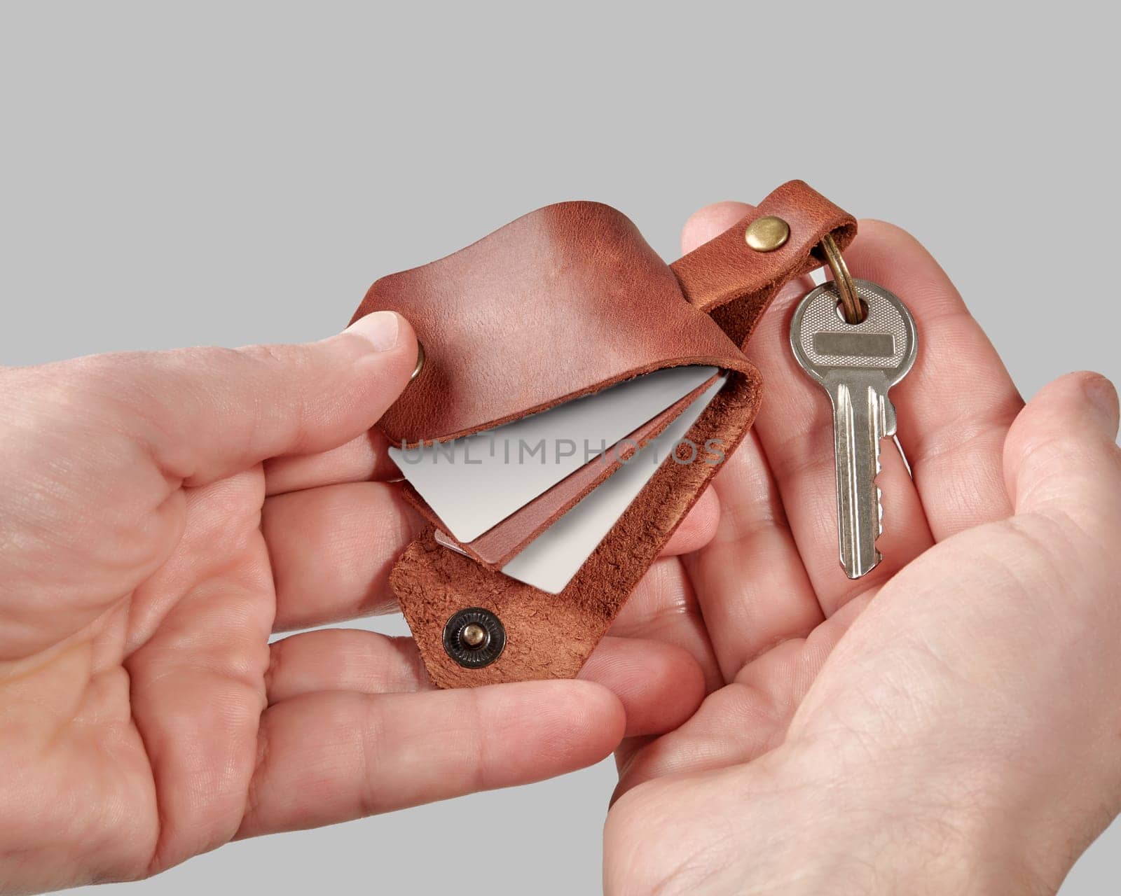 Male hands presenting handcrafted brown leather keychain engraved with DADDY with printed family photos against grey background. Concept of thoughtful personalized gift