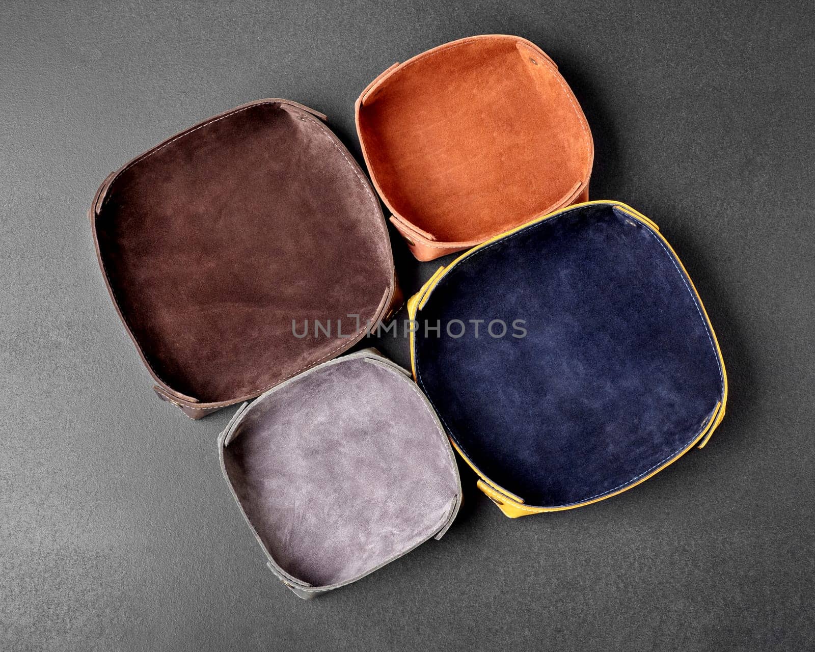 Top view of functional handmade genuine leather catchall trays of different colors and sizes with embossed suede interior for easy storage of sundries, keys, watch and coins on gray background