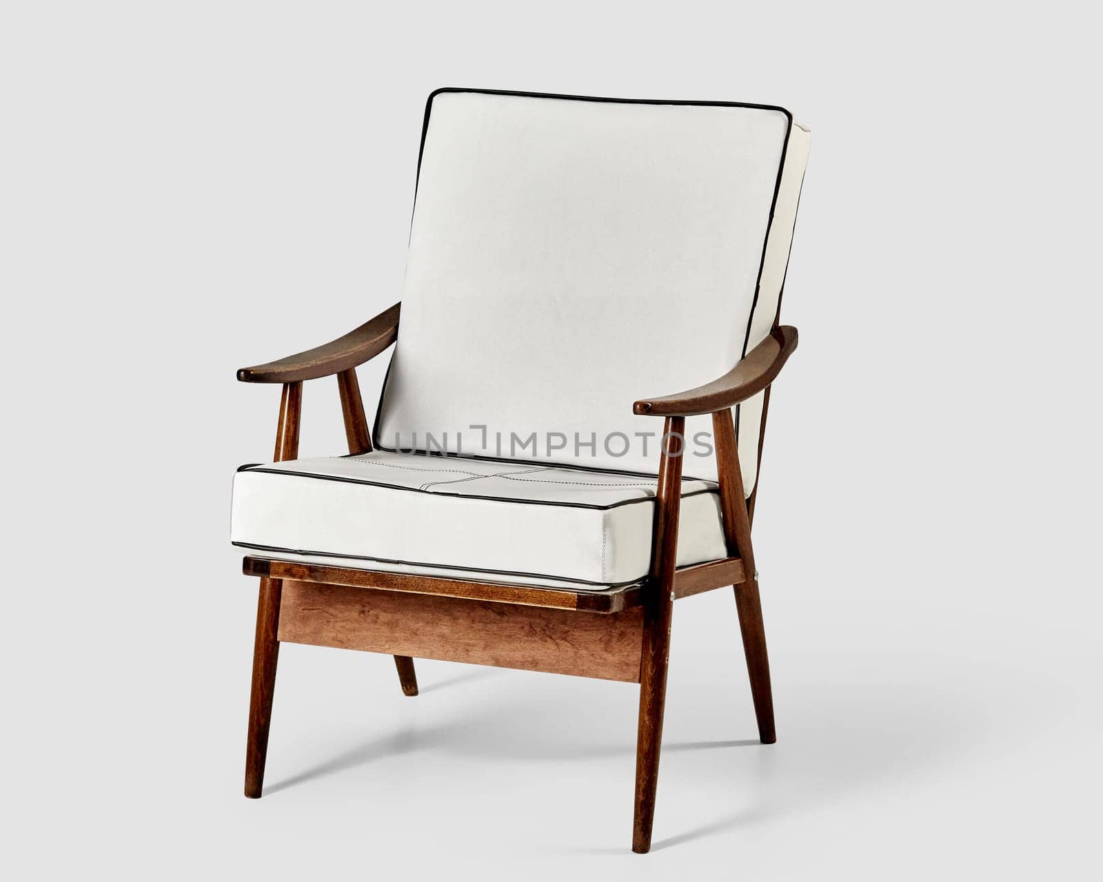 Vintage-inspired wooden chair with sleek white leather upholstery and distinctive armrests, against light backdrop. Stylish piece of furniture for cozy interio