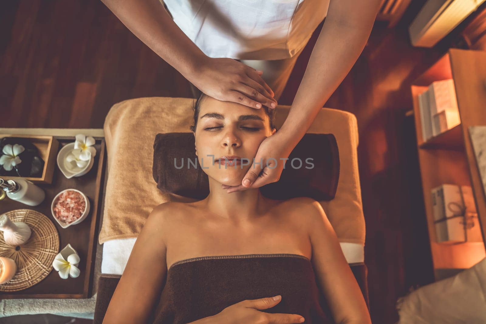 Caucasian woman enjoying relaxing anti-stress head massage and pampering facial beauty skin recreation leisure in warm candle lighting ambient salon spa in luxury resort or hotel. Quiescent