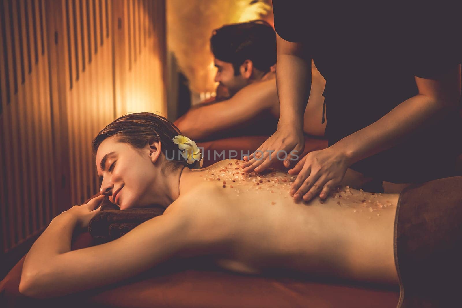 Couple customer having exfoliation treatment in luxury spa salon with warmth candle light ambient. Salt scrub beauty treatment in Health spa body scrub. Quiescent