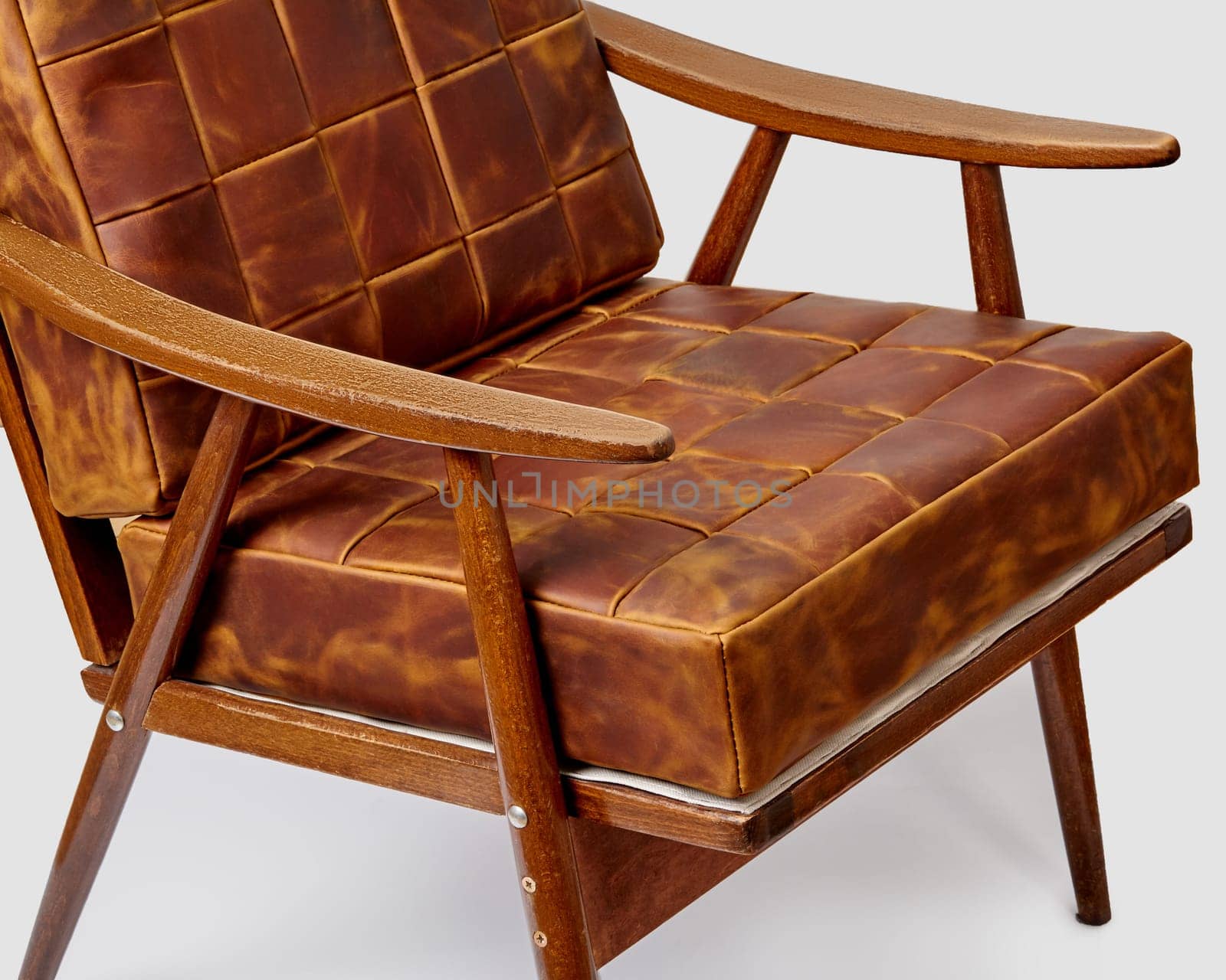 Closeup of high-quality padded soft cushions made of neatly stitched patches of patinated brown leather complementing vintage style wooden chair, blending luxury with comfort