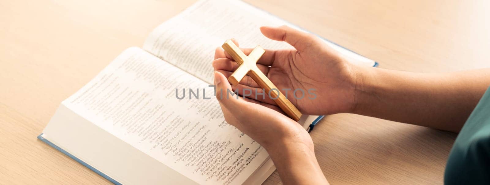Female god believer holding wooden cross on opened holy bible book at light wooden church table. Top view. Concept of hope, religion, faith, christianity and god blessing. Warm background. Burgeoning.