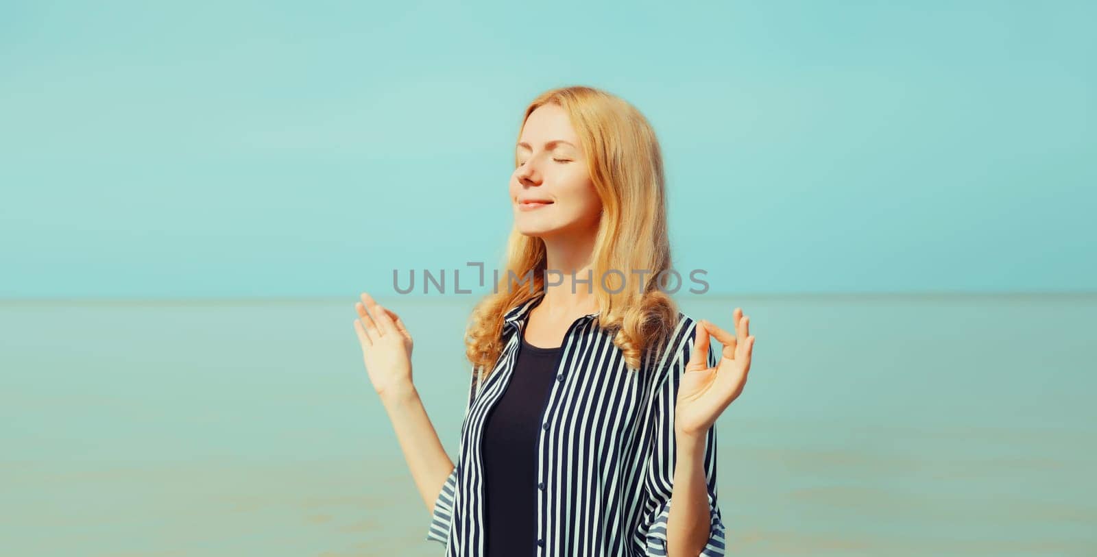 Calm relaxing healthy young woman meditates, practicing yoga enjoying fresh air on the beach on sea coast and blue sky background