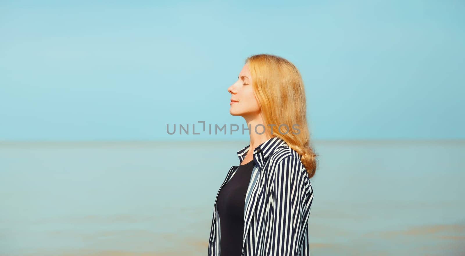 Calm relaxing healthy young woman meditates, practicing breathing exercises enjoying fresh air on the beach on sea coast and blue sky background