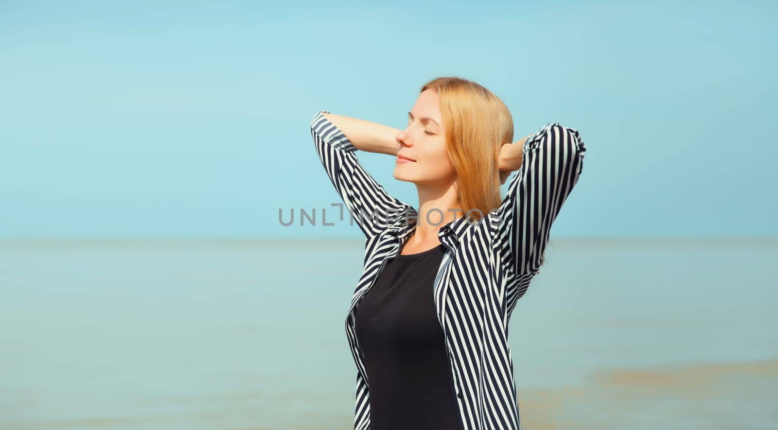 Summer vacation, happy relaxing healthy young woman meditates and enjoying fresh air on the beach on sea coast and blue sky background