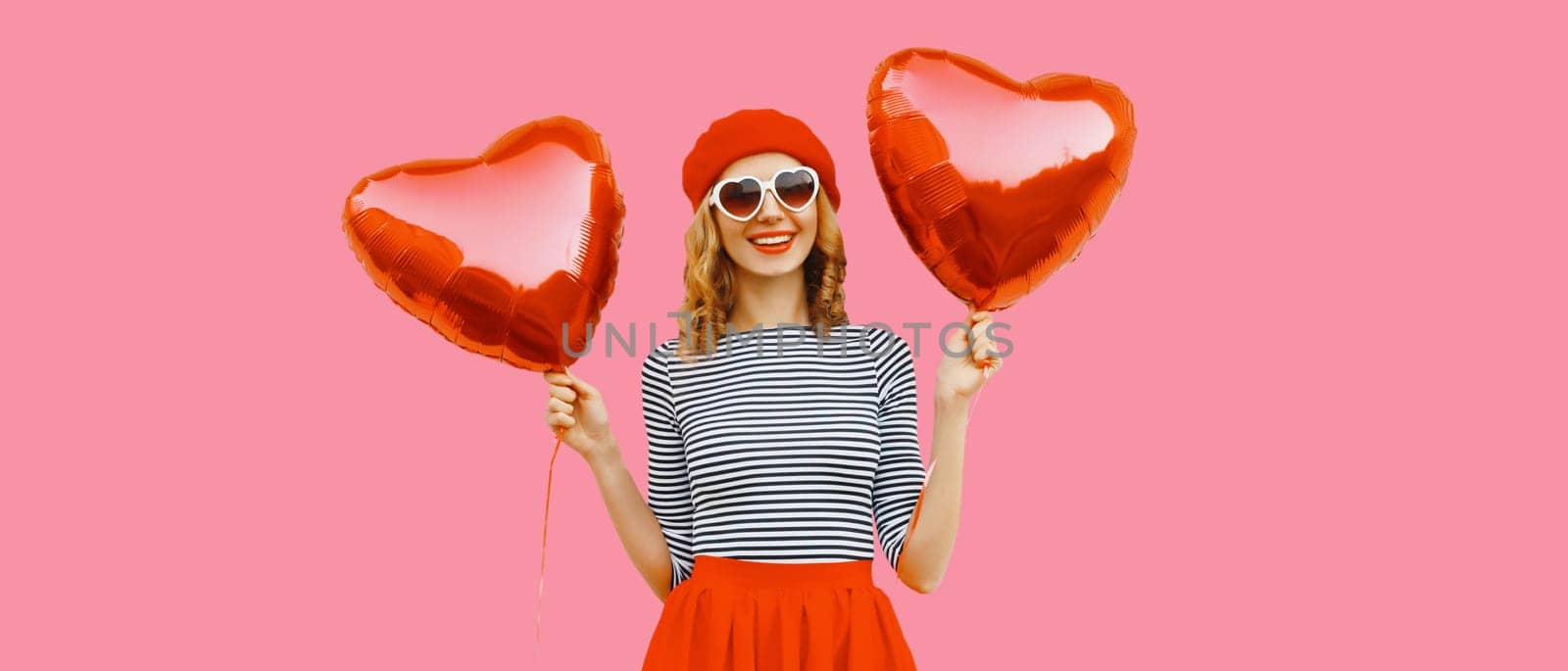 Cute portrait of happy cheerful smiling young woman with red heart shaped balloon wearing french beret hat on pink studio background