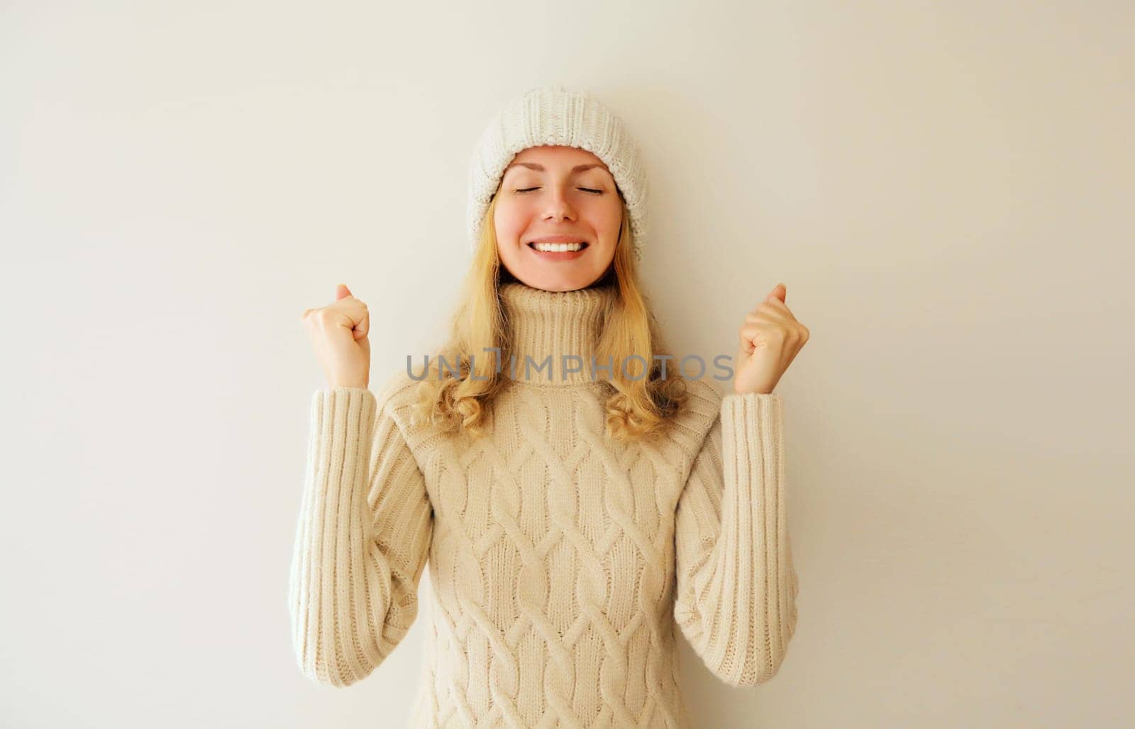 Overjoyed happy woman doing winner gesture celebrate clenching fists say yes expressing emotions of joy and victory win in knitted sweater and hat