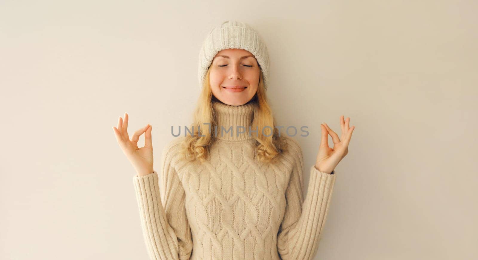 Relaxed happy young woman meditates in yoga position in winter warm knitted sweater and hat by Rohappy