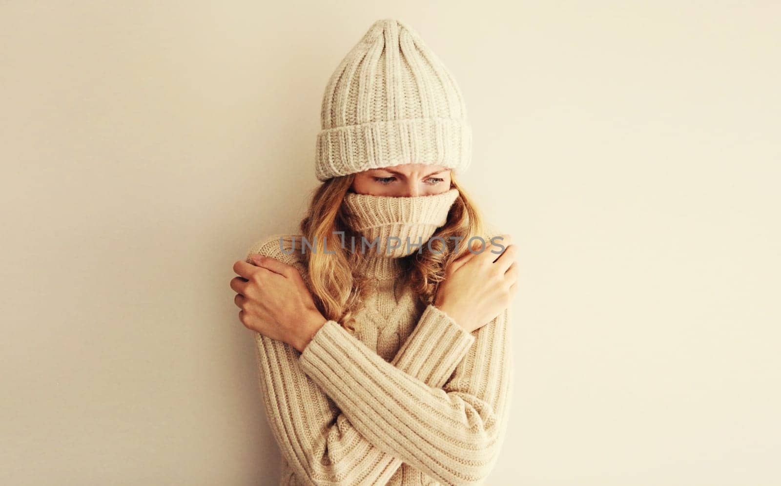 Woman freezing trying to warm up in winter warm knitted clothes, hat and sweater at home