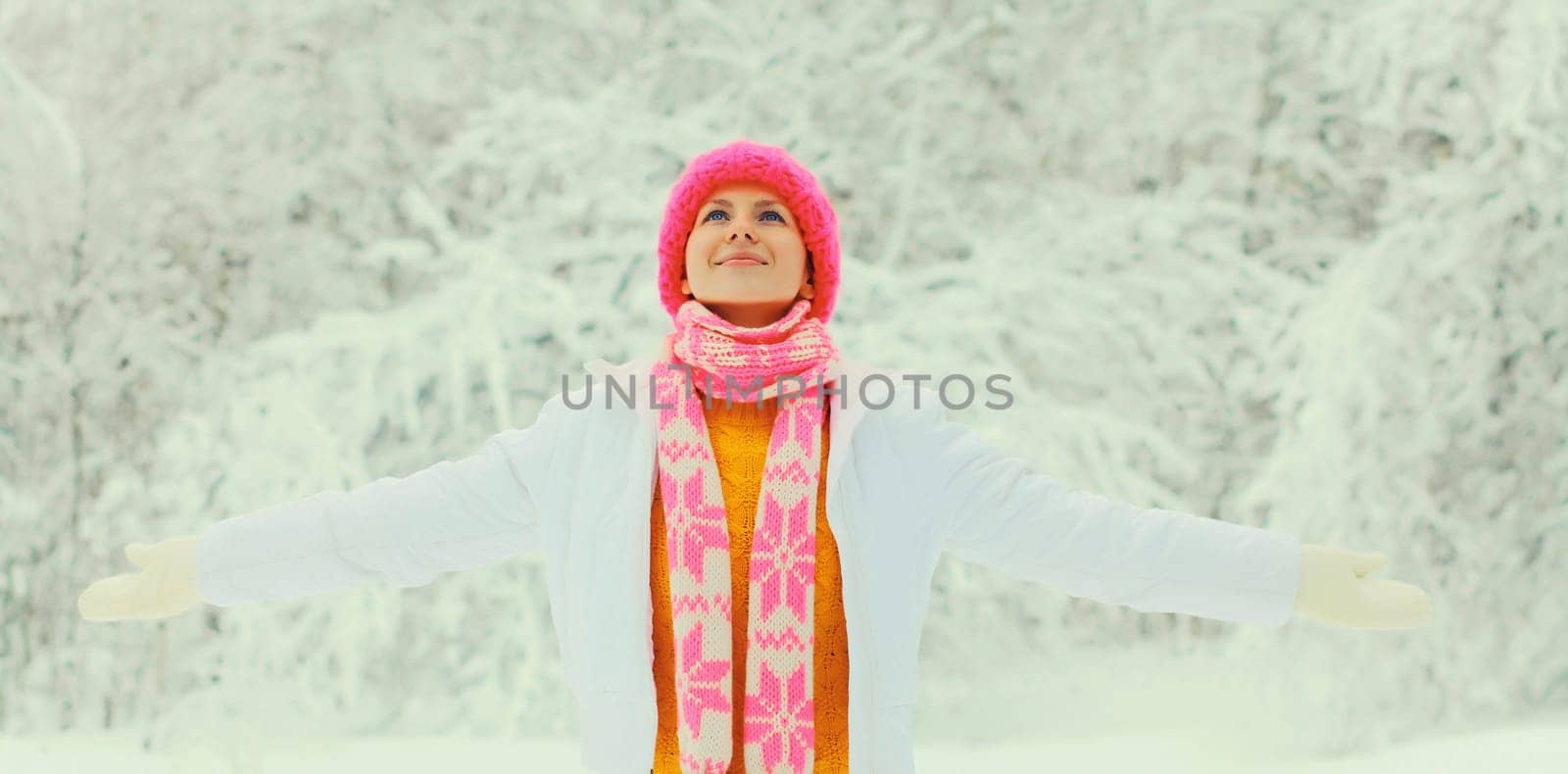 Winter portrait of happy smiling young woman in colorful knitted hat, scarf enjoys weather on snowy forest park background