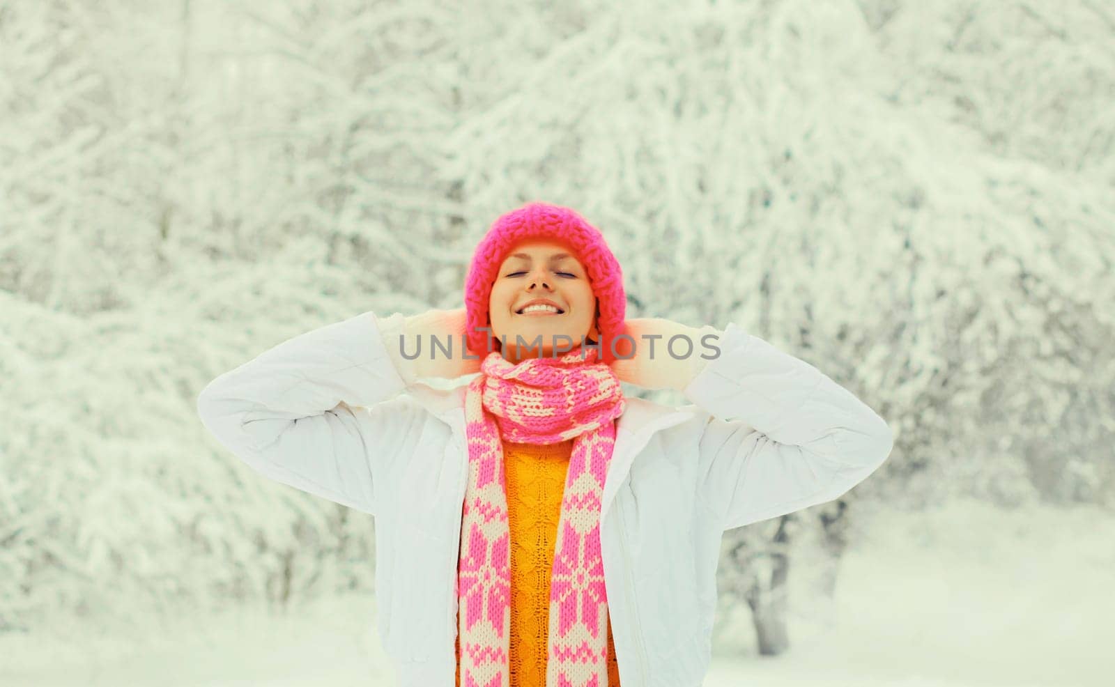 Winter portrait of happy smiling young woman in colorful knitted hat, scarf enjoys weather on snowy forest park background