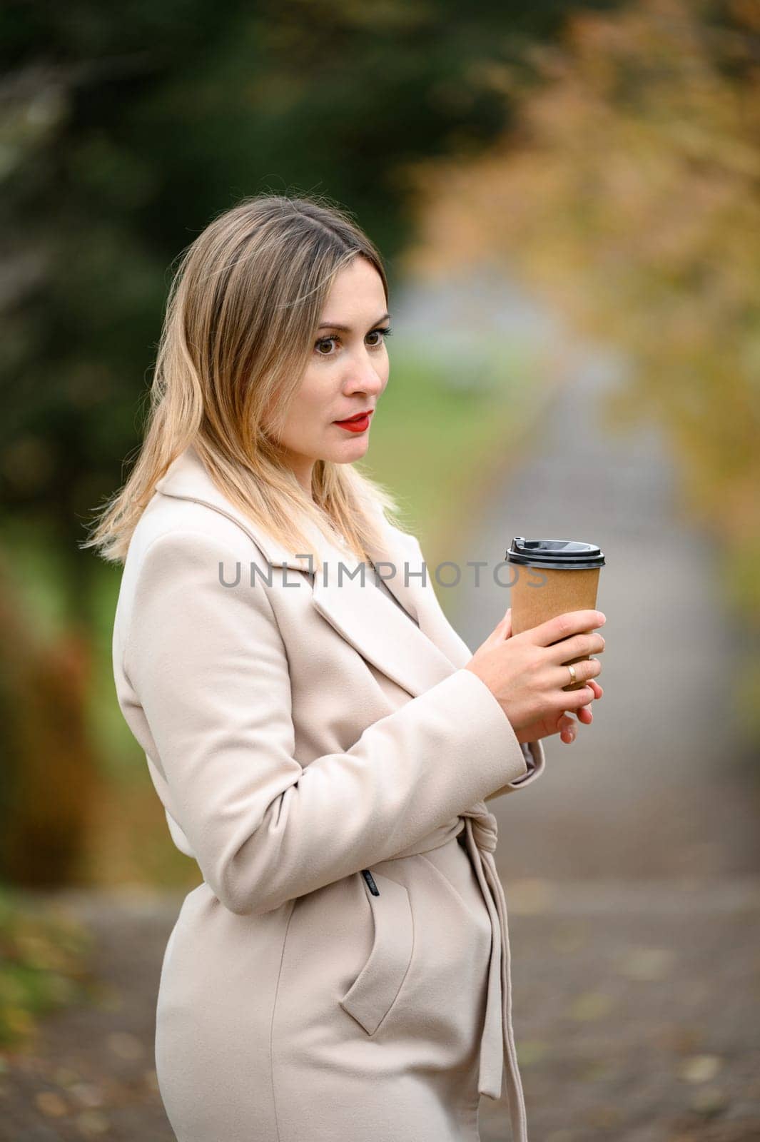 A young girl in the autumn park drinks coffee, rest in the park.