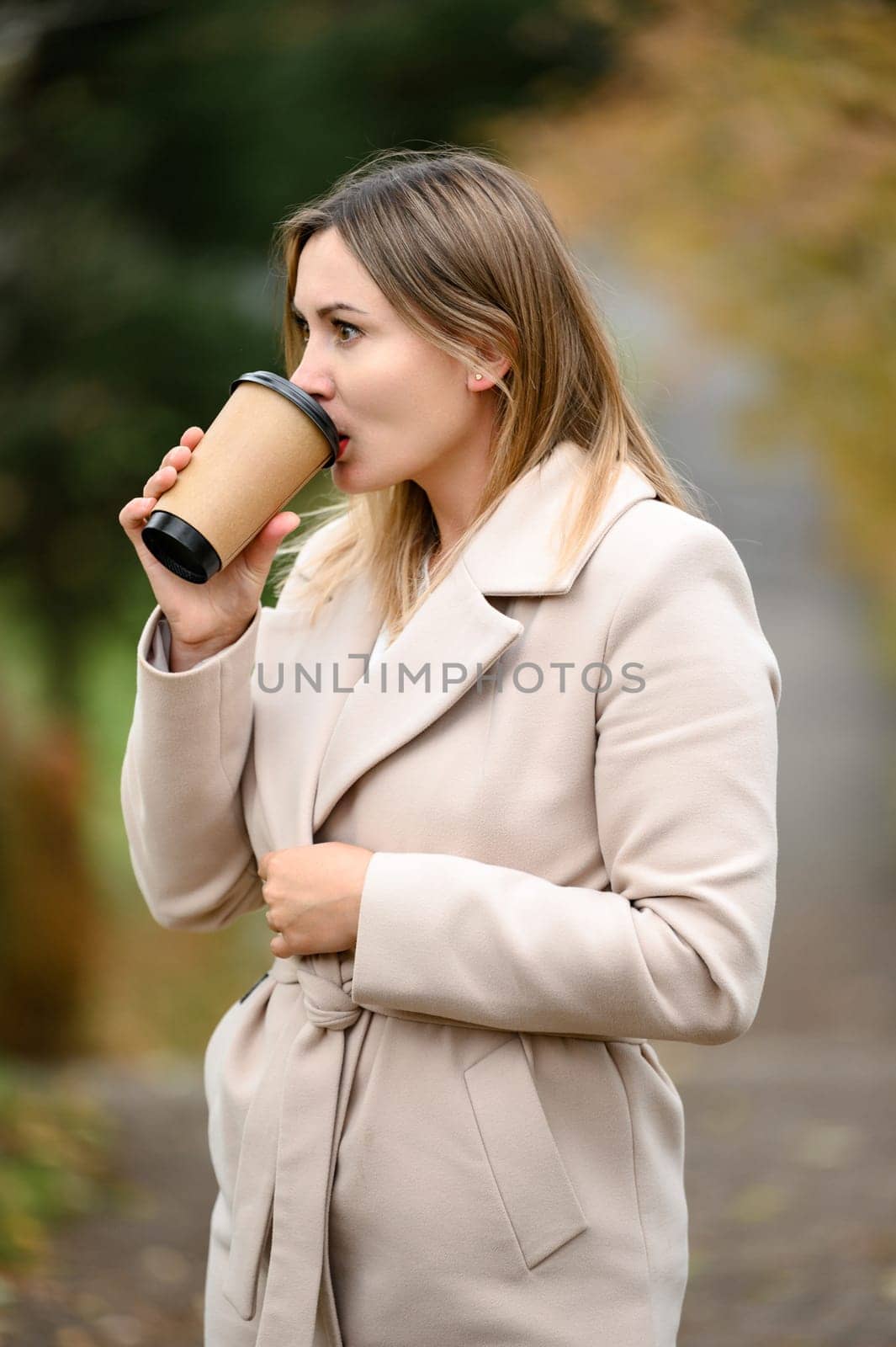 A young girl in the autumn park drinks coffee. by Niko_Cingaryuk