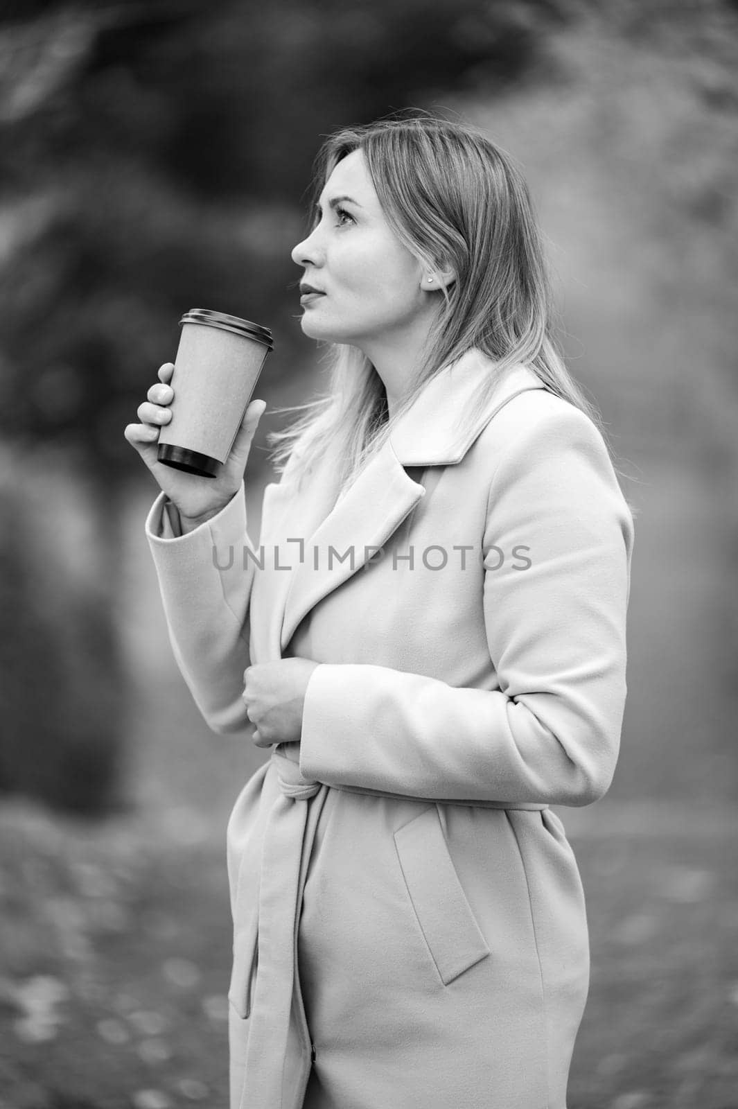 A young girl in the autumn park drinks coffee, rest in the black and white park.