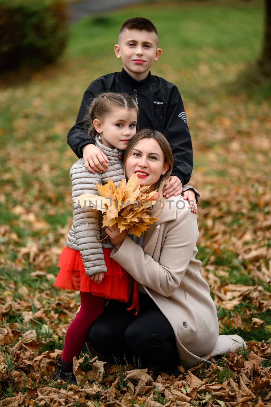 Portrait of mother with daughter and son in autumn park with leaves, happy motherhood.