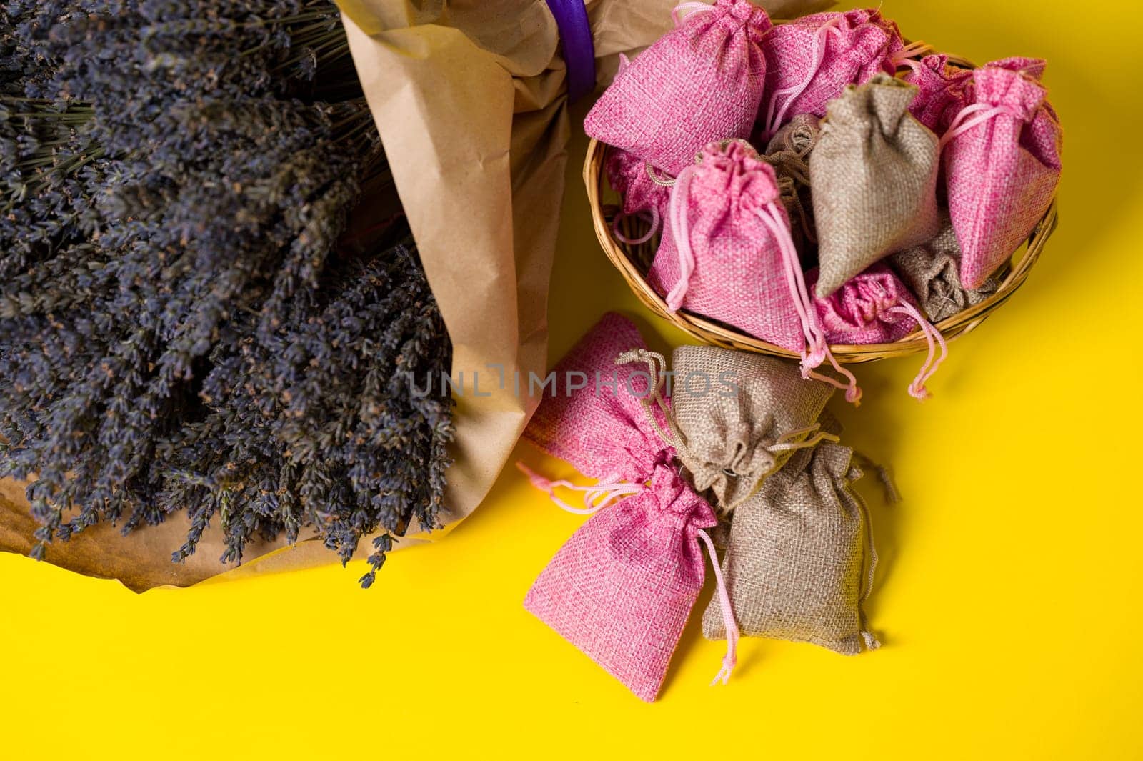 Dried lavender flowers and sachets on yellow background, lavender aromatherapy.