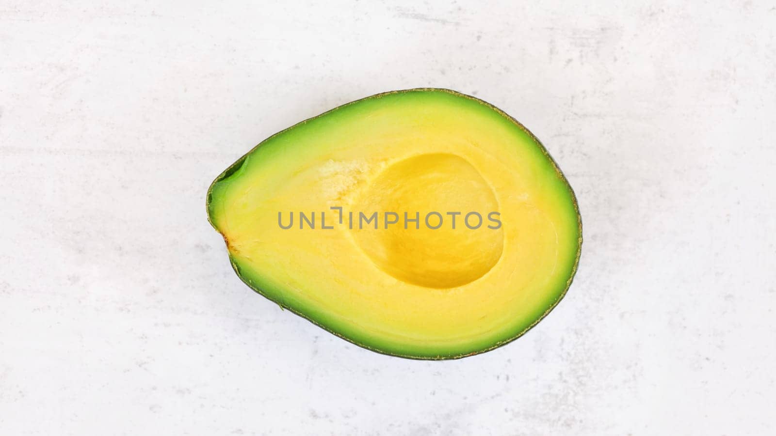 Avocado half, with bright yellow pulp on white stone board, photo from above by Ivanko