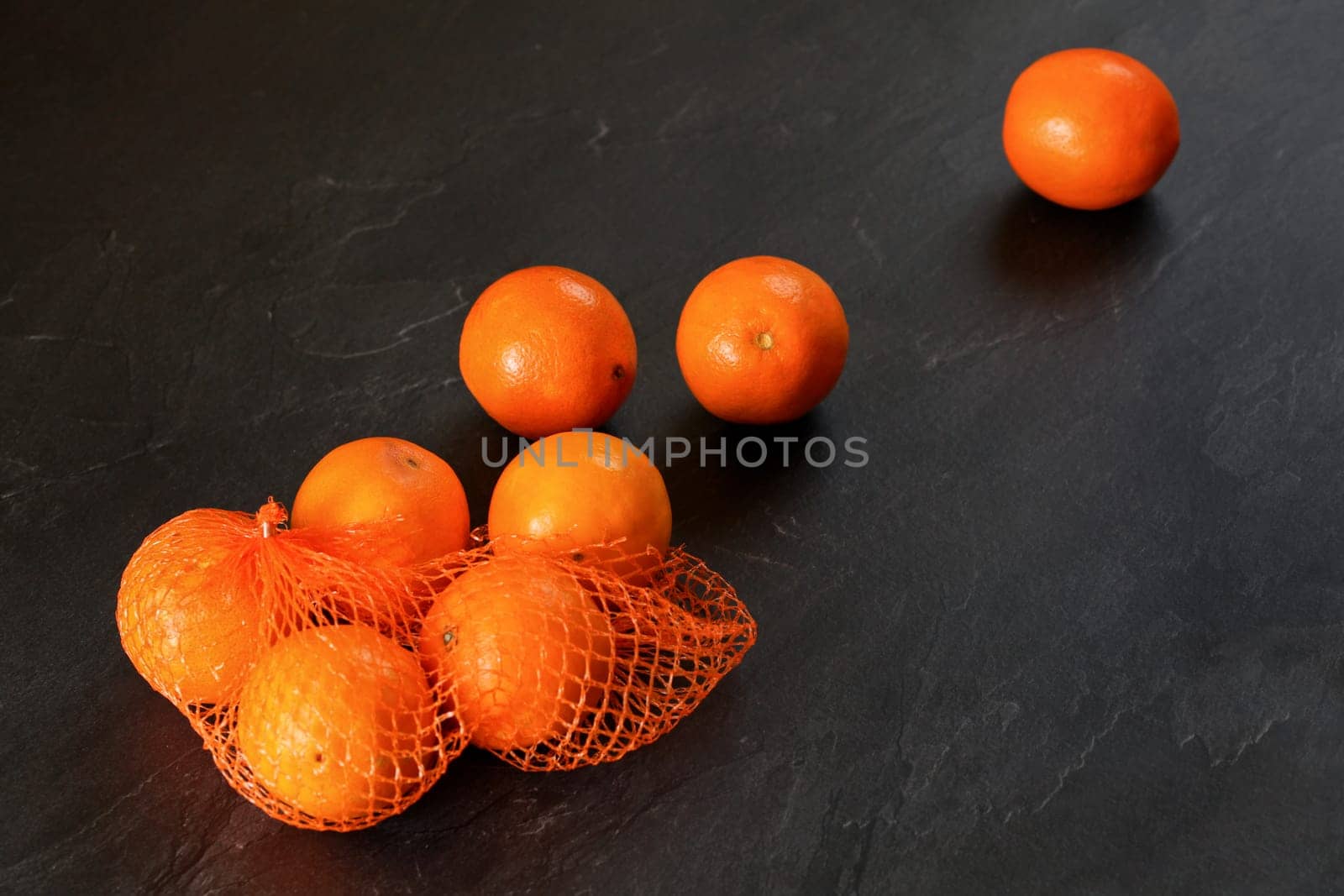 Oranges in red plastic net, some scattered on black stone like board
