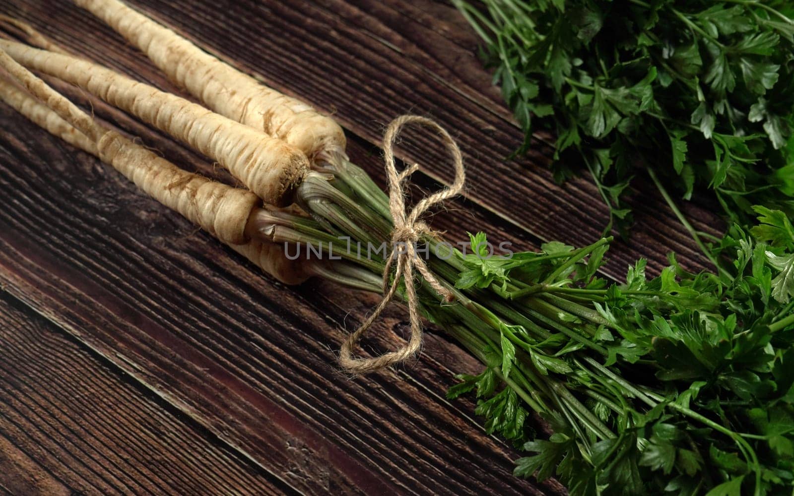 Bunch of white parsnip roots with green leaves on dark wooden rustic board, photo from above
