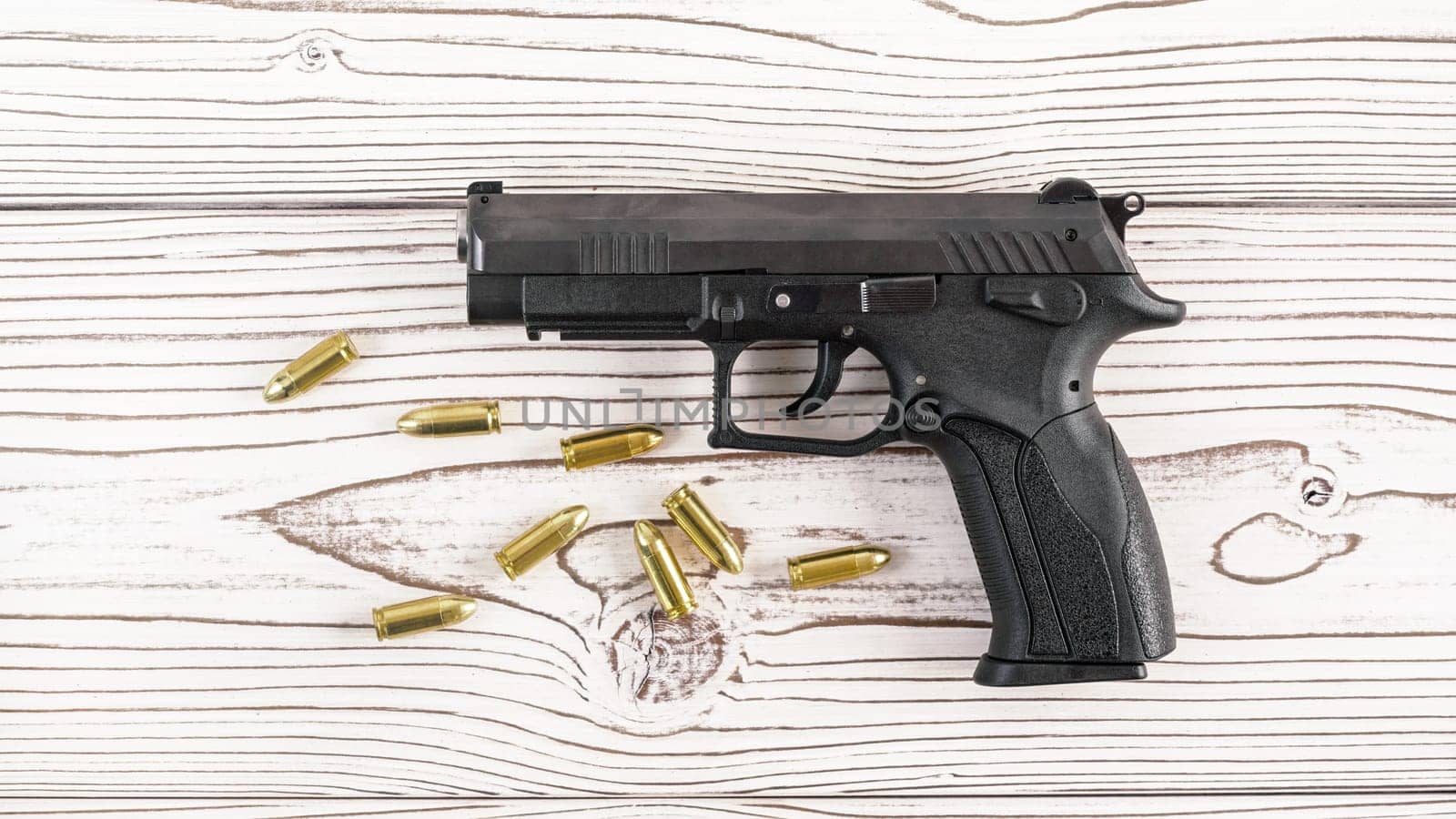 Simple black modern pistol gun with few yellow brass bullets on white wooden board, view from above
