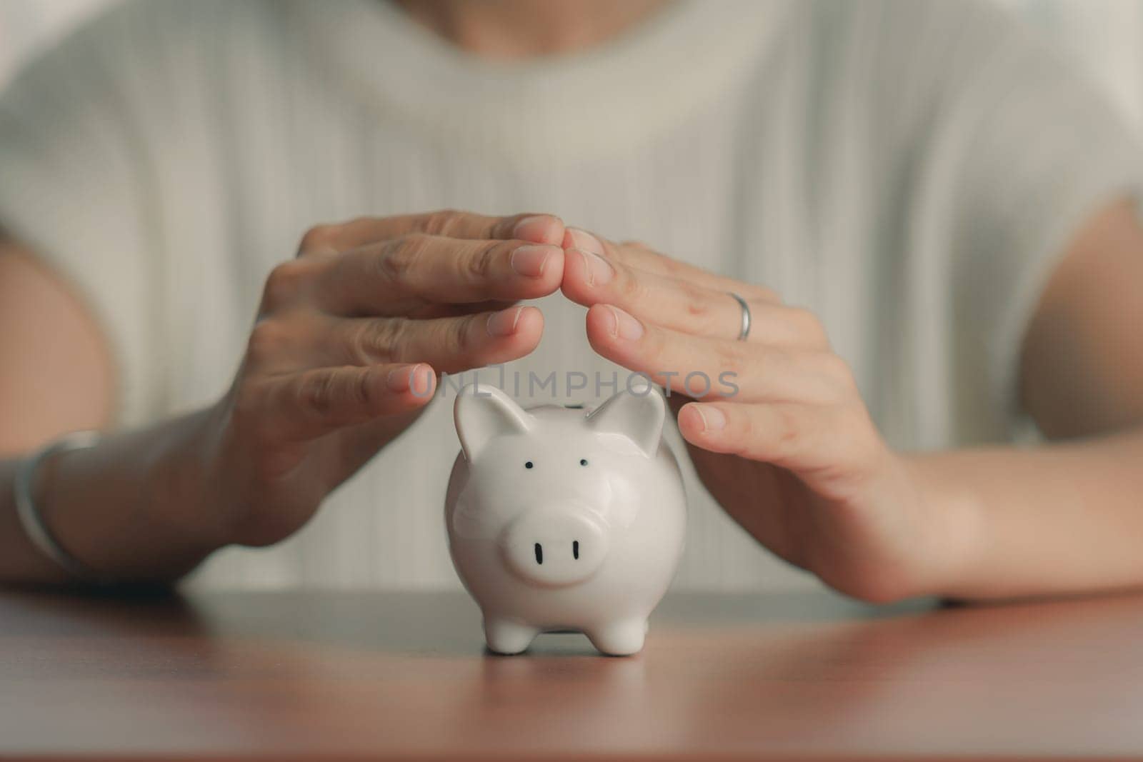 Woman hands covering piggy bank and saving money by iamnoonmai