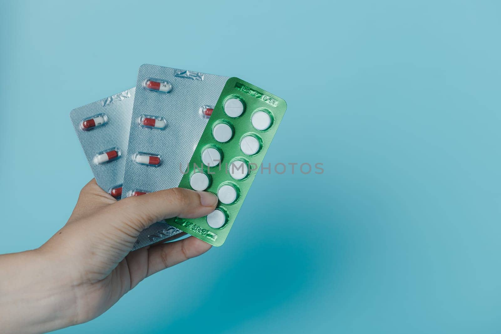 Female hand holding a pack of pills on a blue background with copy space for medical and healthcare concept