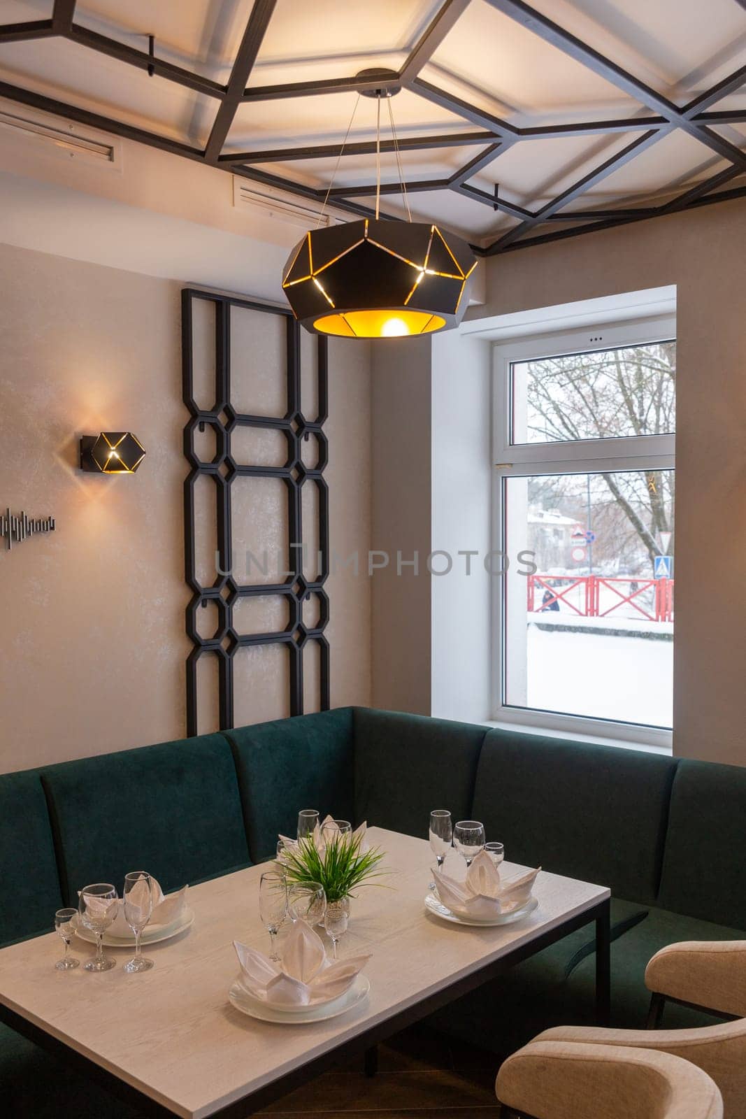 Modern interior of urban restaurant or cafe with dining places. Soft green sofas and beige chairs around tables served with glasses, plates and napkins.