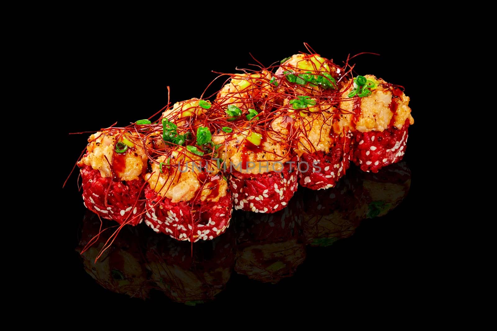 Exquisite red rice sushi rolls crowned with seared cheese caps with scallops, adorned with togarashi threads, green onion, and drizzle of unagi sauce, presented on reflective black surface