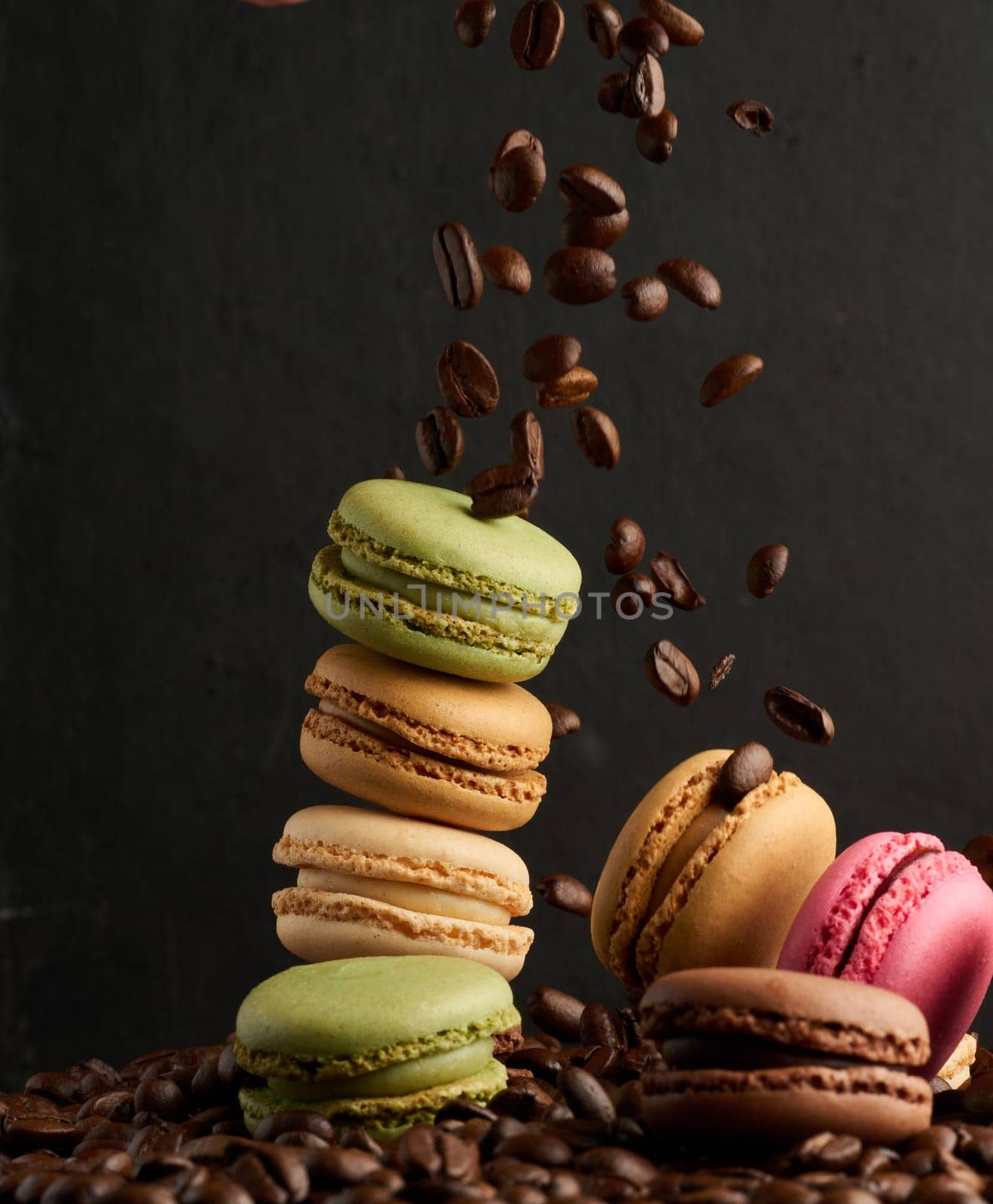 Stack of colorful macarons and flying coffee beans on a black background by ndanko