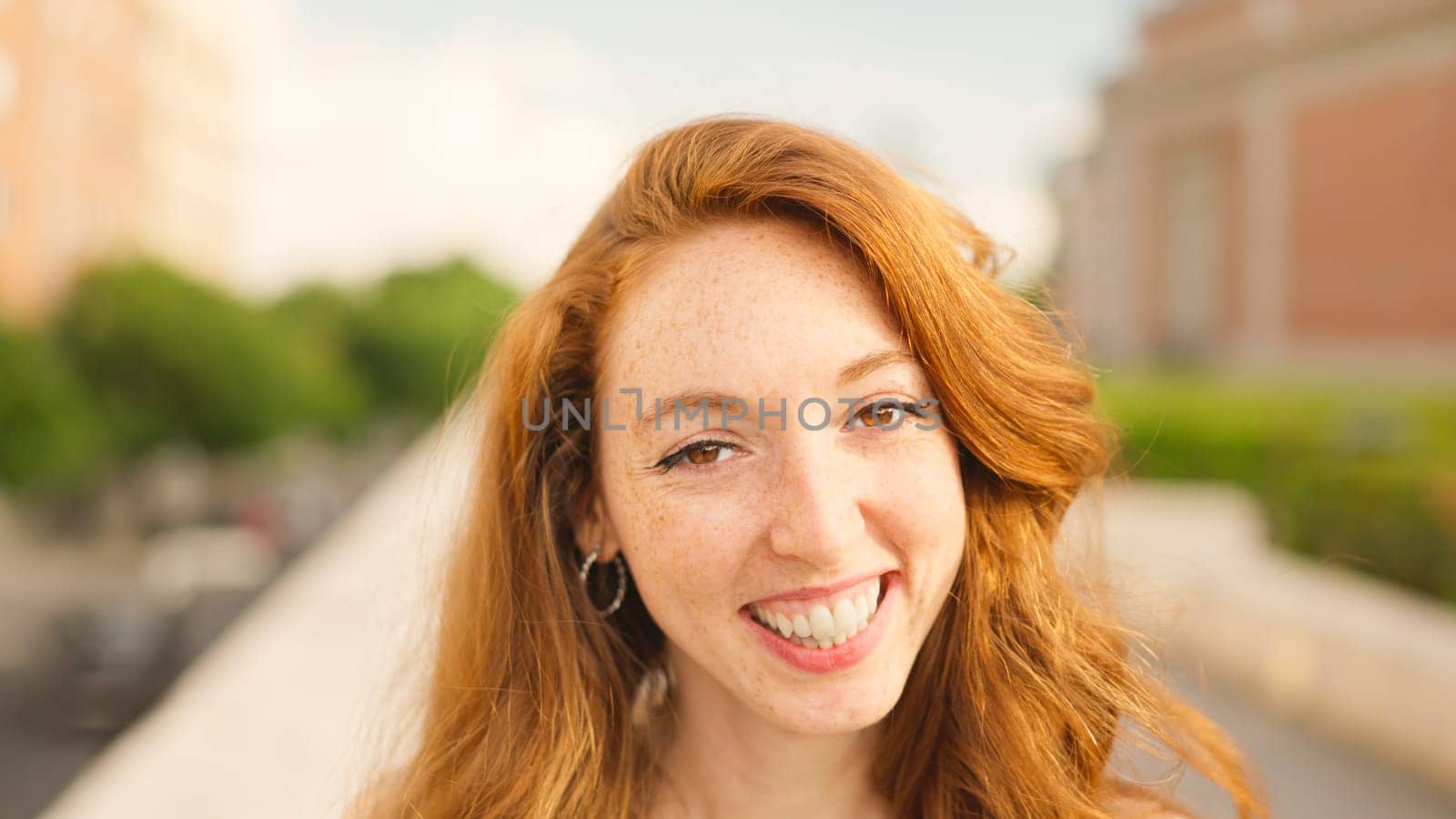 Red haired caucasian adult woman looks at camera and smiles in the street