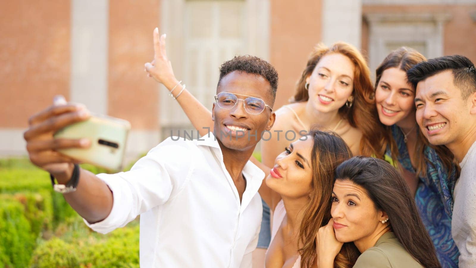 Multicultural group of friends smiling while taking a selfie with a mobile in the street