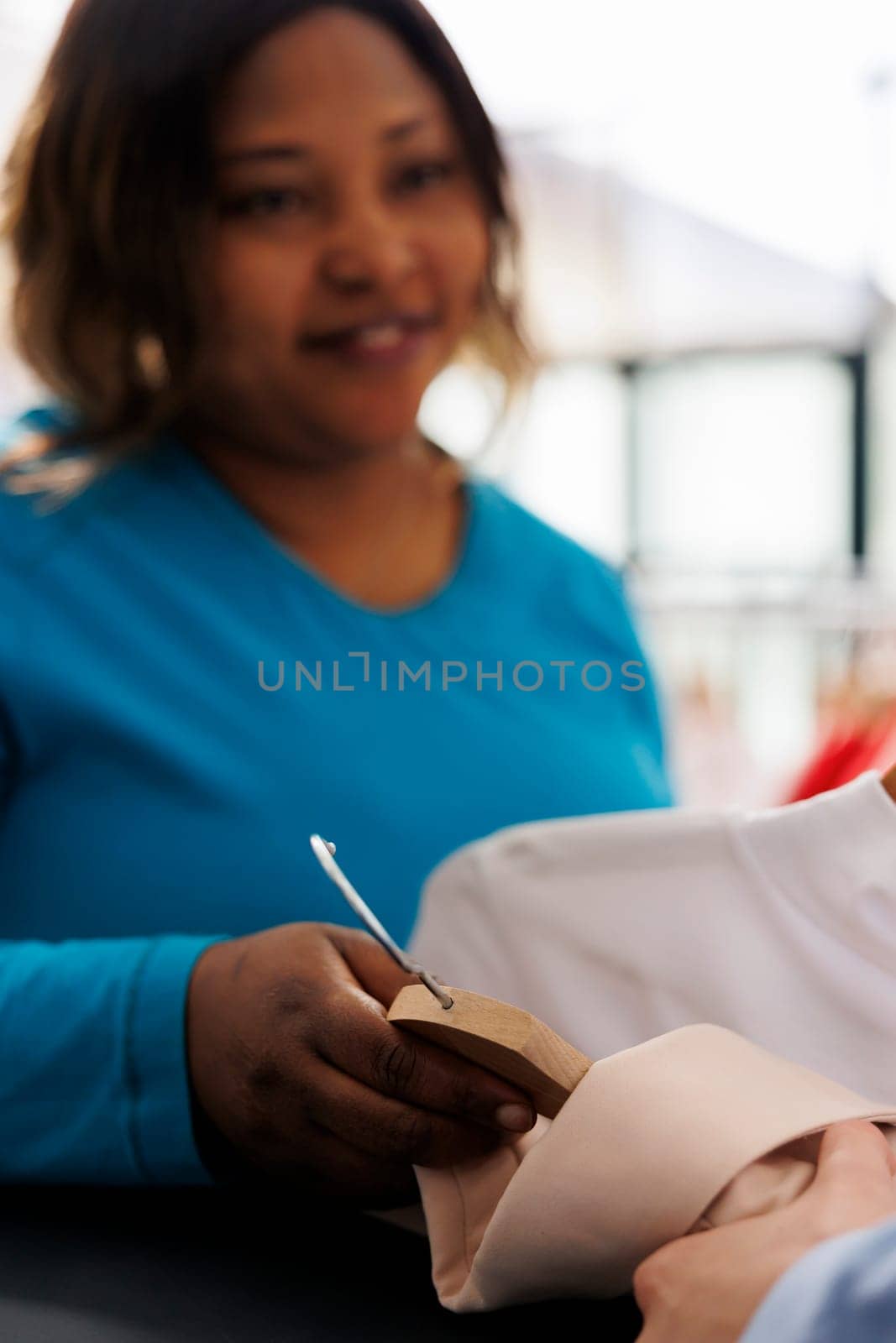 African american woman holding multiple shirts, buying stylish clothes in modern boutique. Smiling shopper wanting new wardrobe, shopping for fashionable merchandise and accessories