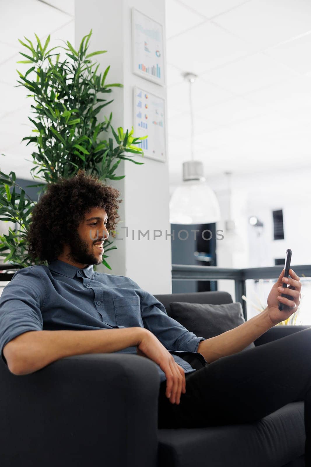 Smiling start up company employee chatting online on mobile phone while working in unicorn business office. Relaxed young arab executive manager talking on smartphone videocall during break