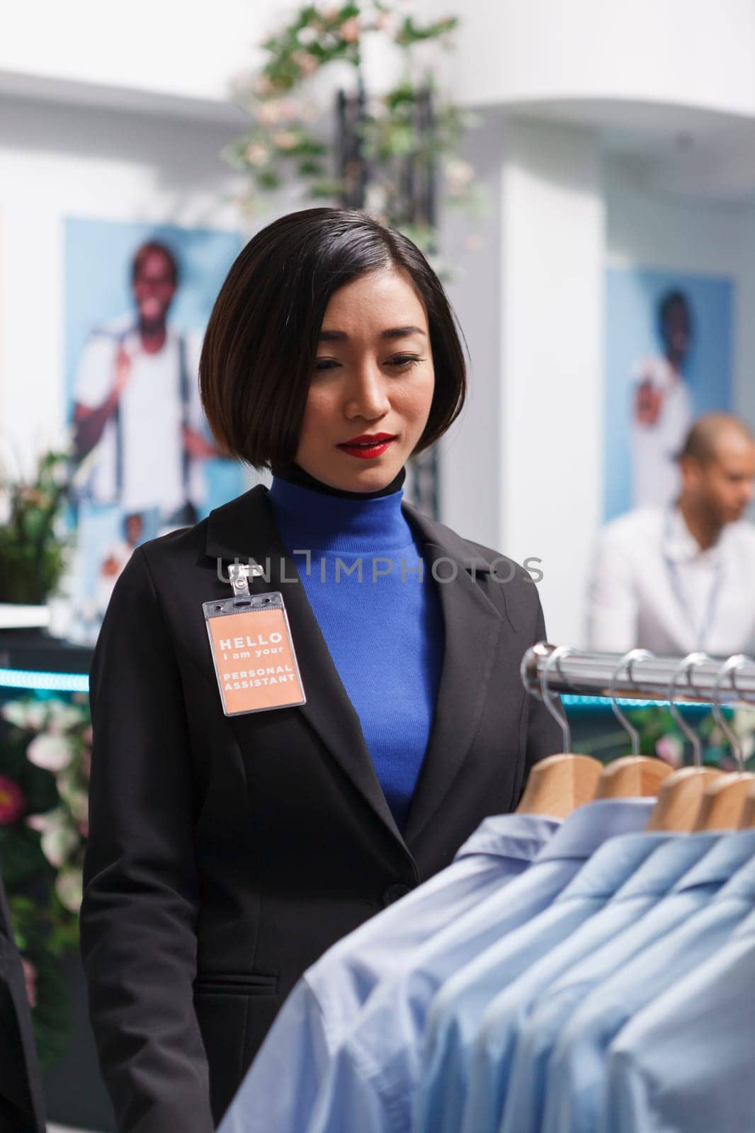 Boutique asian woman employee examining shirts on rack, organizing merchandise and managing inventory. Shopping mall clothing store seller checking hanging apparel in stock