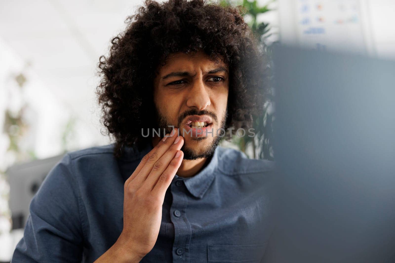 Young arab employee with toothache having online chat with dentist at workplace. Entrepreneur with tooth pain calling doctor on laptop while working in business company office