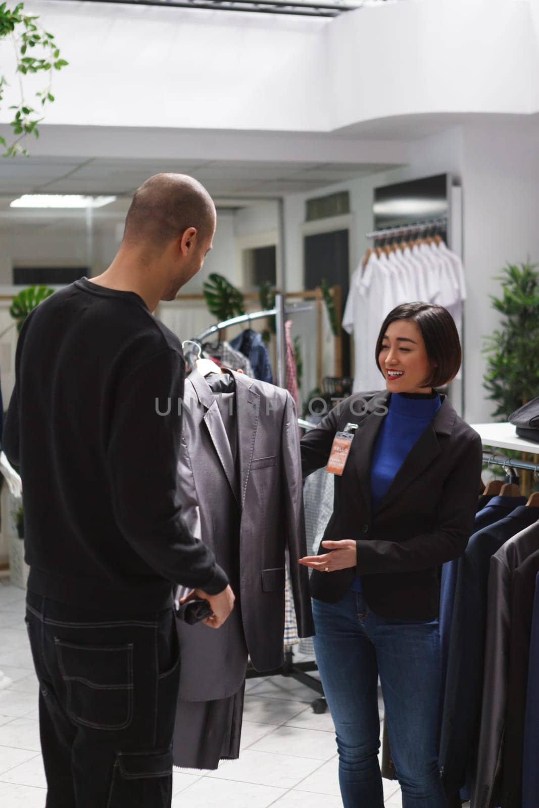 Clothing store assistant offering guidance to arab man client in choosing apparel style and fit. Shopping center fashion department worker consulting customer in selecting jacket