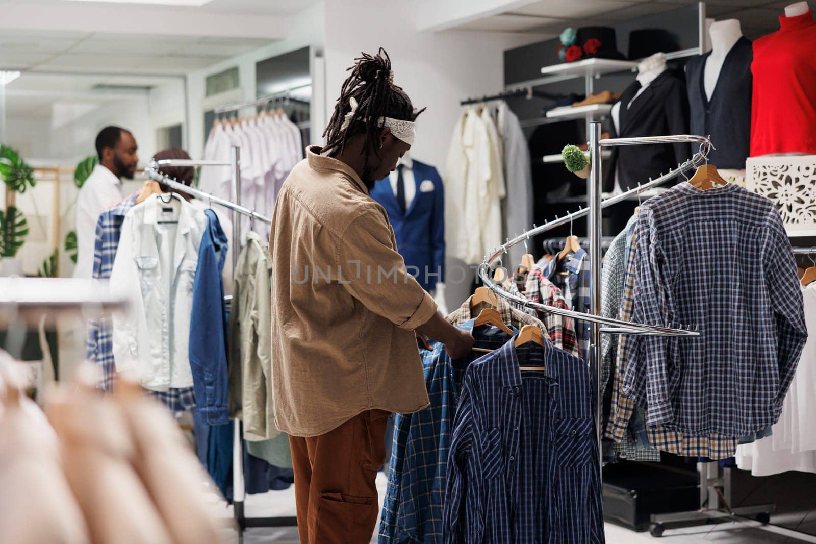 Client looking at hanging shirts on rack in boutique. by DCStudio