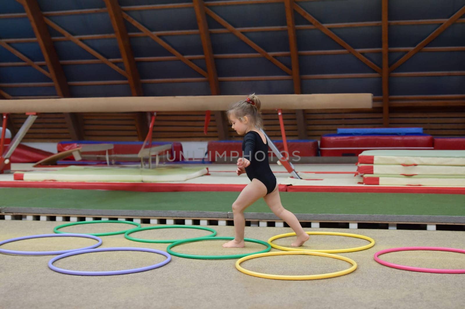 A three-year-old girl runs through hula hoops in the gym