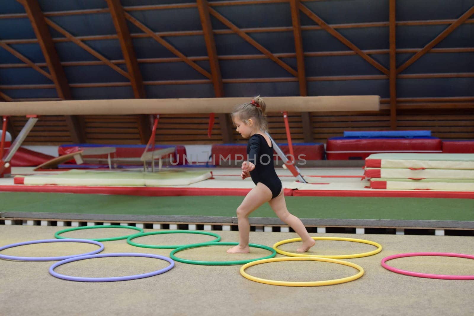 A small girl runs through hula hoops in the gym by Godi