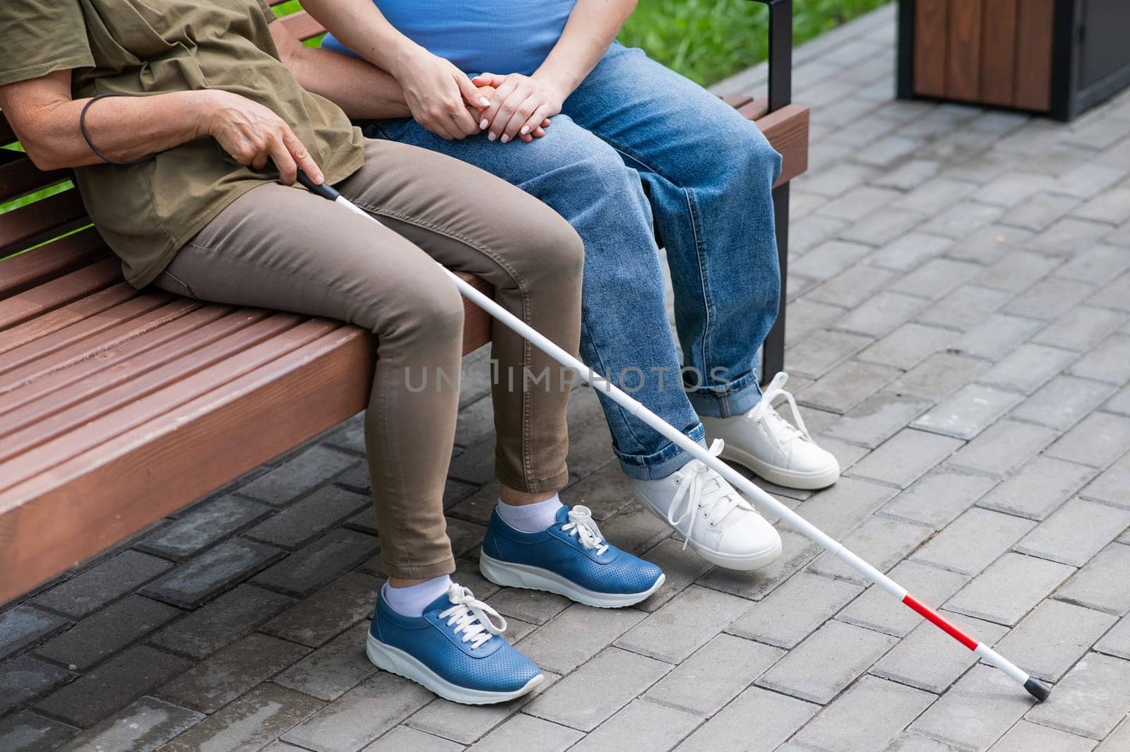 An elderly blind woman and her pregnant daughter are sitting on a bench in the park. Close up legs