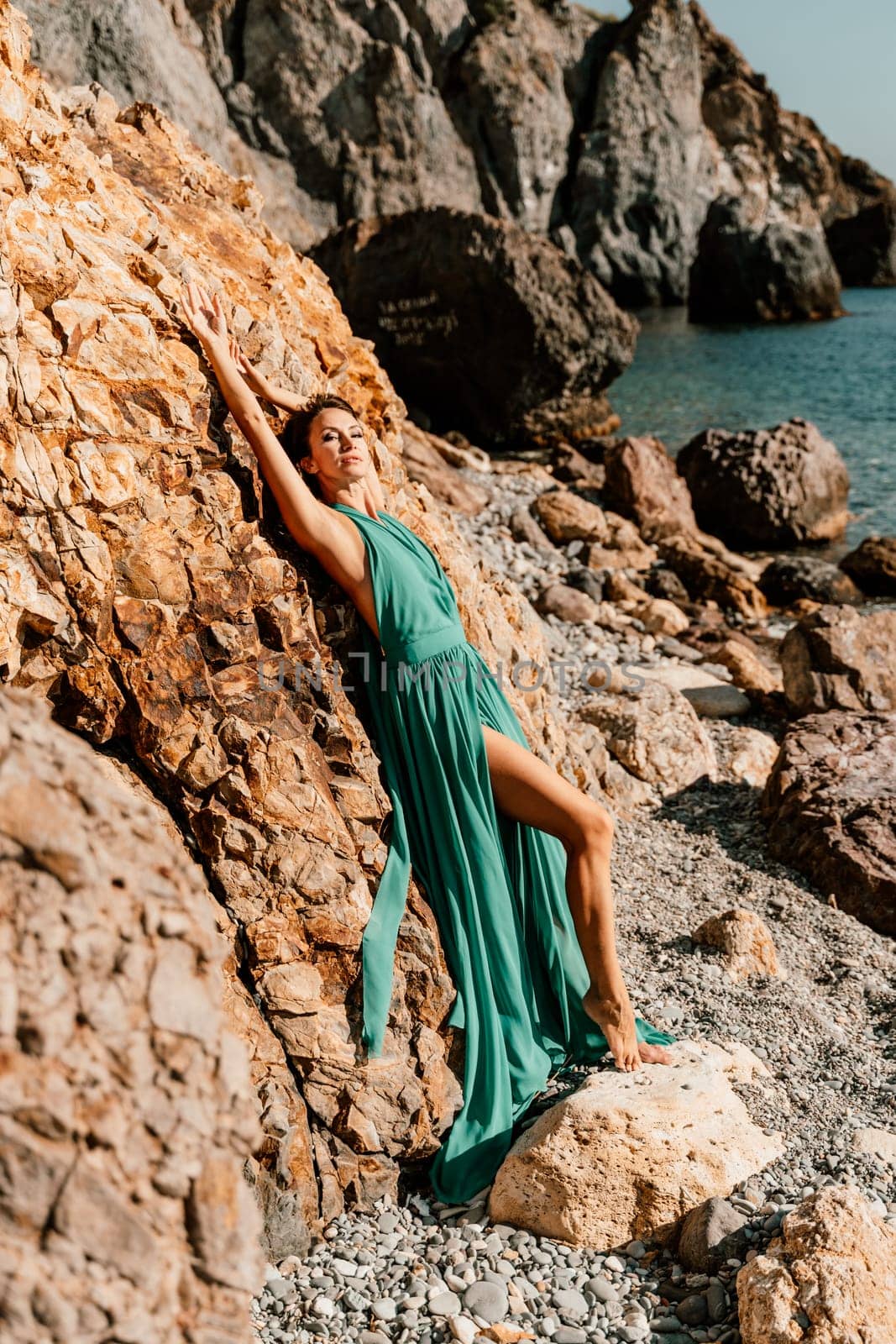 Woman green dress sea. Woman in a long mint dress posing on a beach with rocks on sunny day. Girl on the nature on blue sky background. by Matiunina