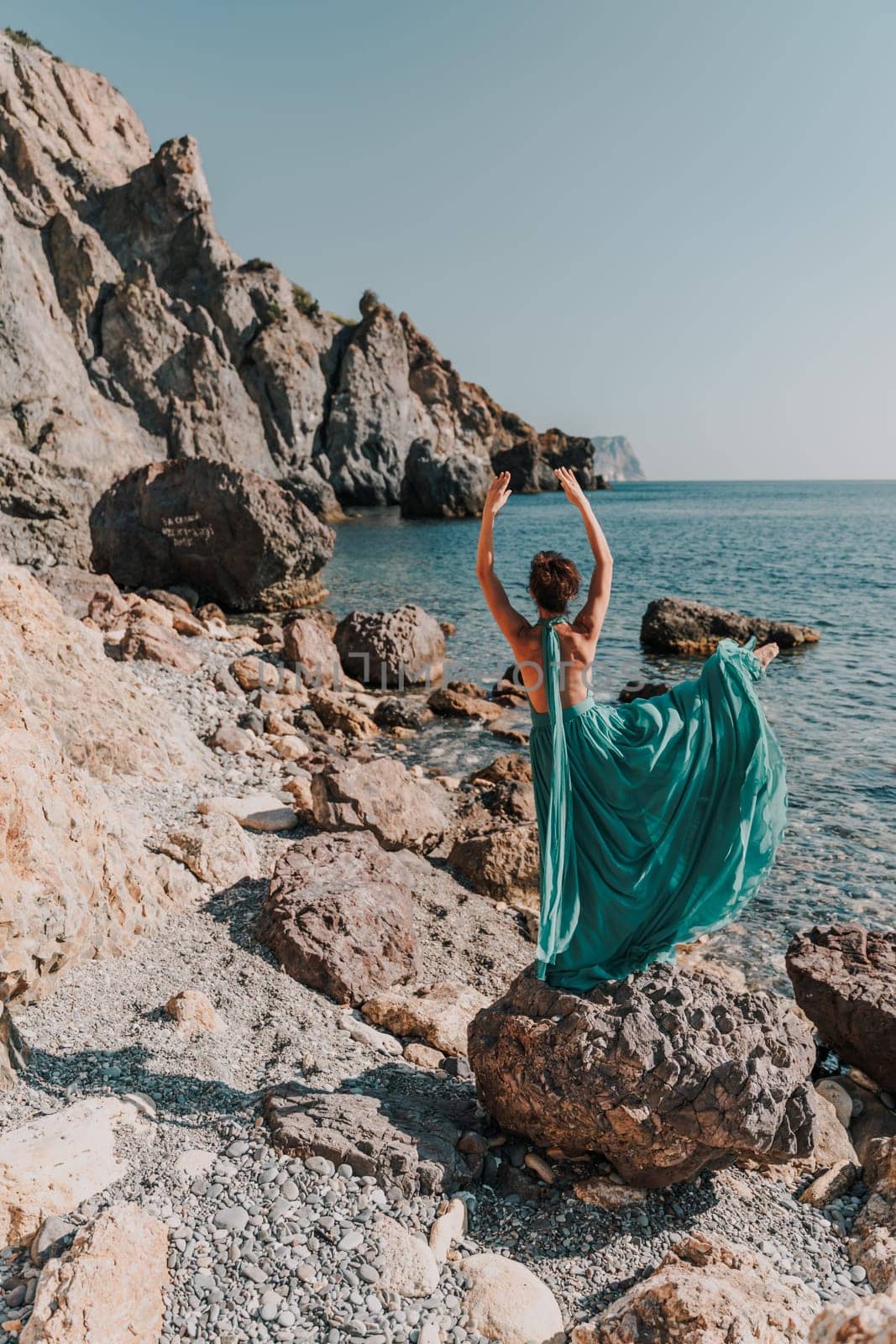 Woman green dress sea. Woman in a long mint dress posing on a beach with rocks on sunny day. Girl on the nature on blue sky background