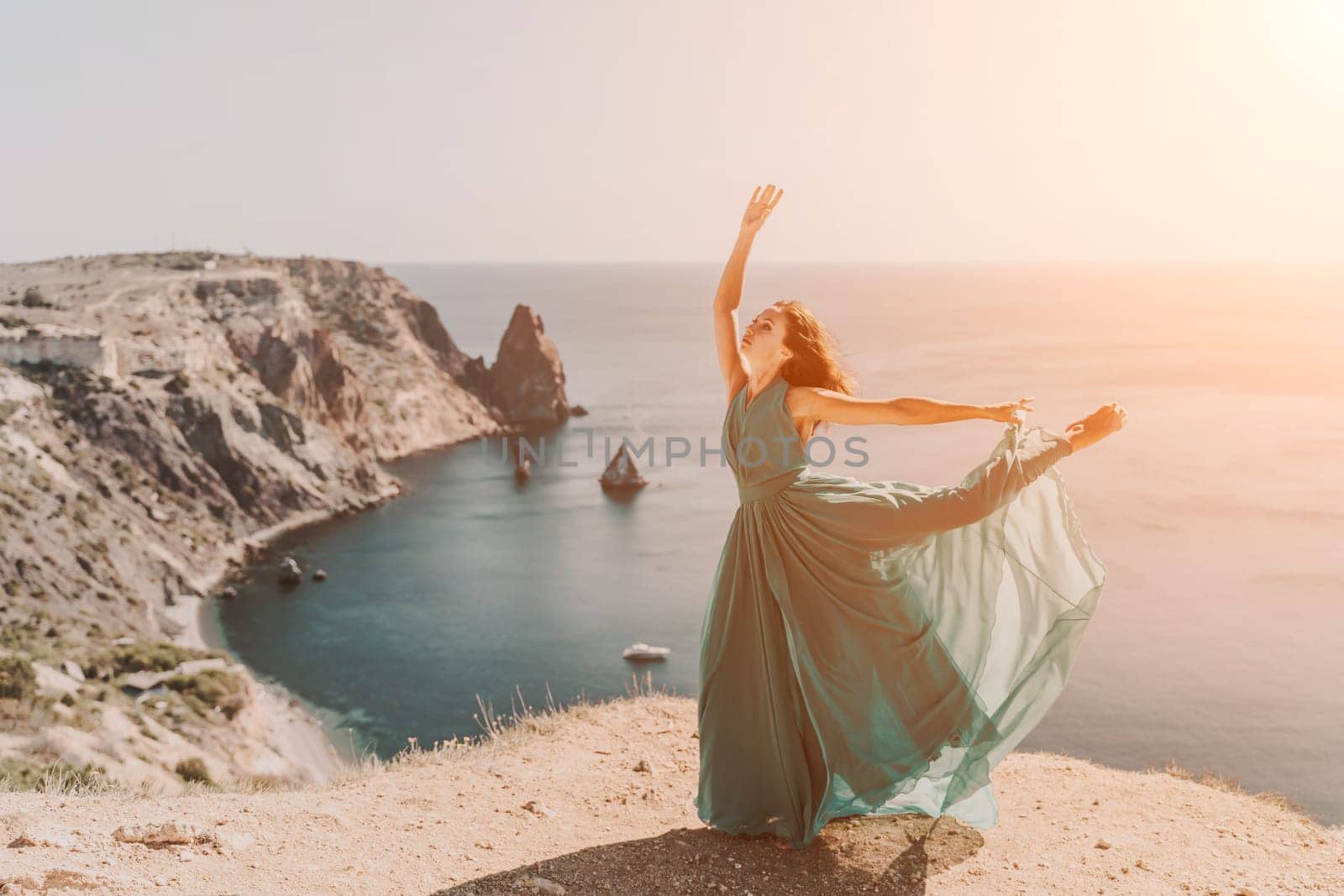 Woman green dress sea. Female dancer posing on a rocky outcrop high above the sea. Girl on the nature on blue sky background. Fashion photo