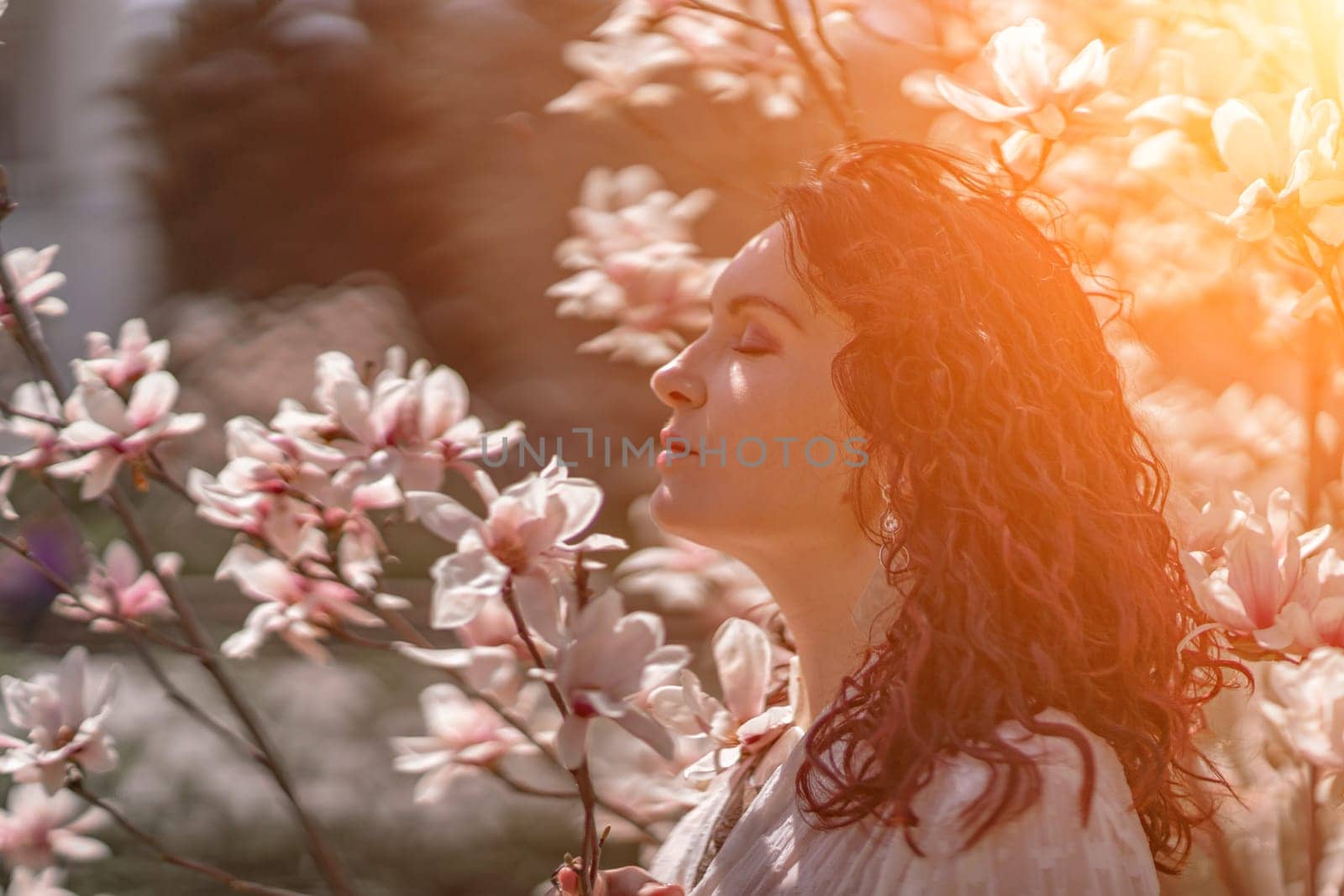 Magnolia park woman. Stylish woman in a hat stands near the magnolia bush in the park. Dressed in white corset pants and posing for the camera. by Matiunina