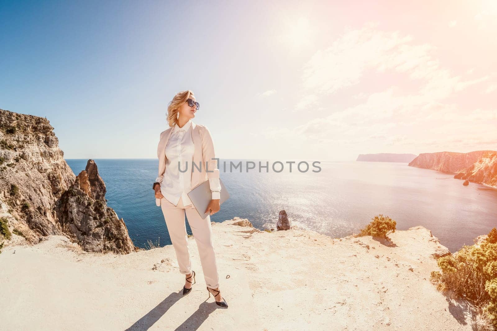 Digital nomad, Business woman working on laptop by the sea. Pretty lady typing on computer by the sea at sunset, makes a business transaction online from a distance. Freelance, remote work on vacation by panophotograph