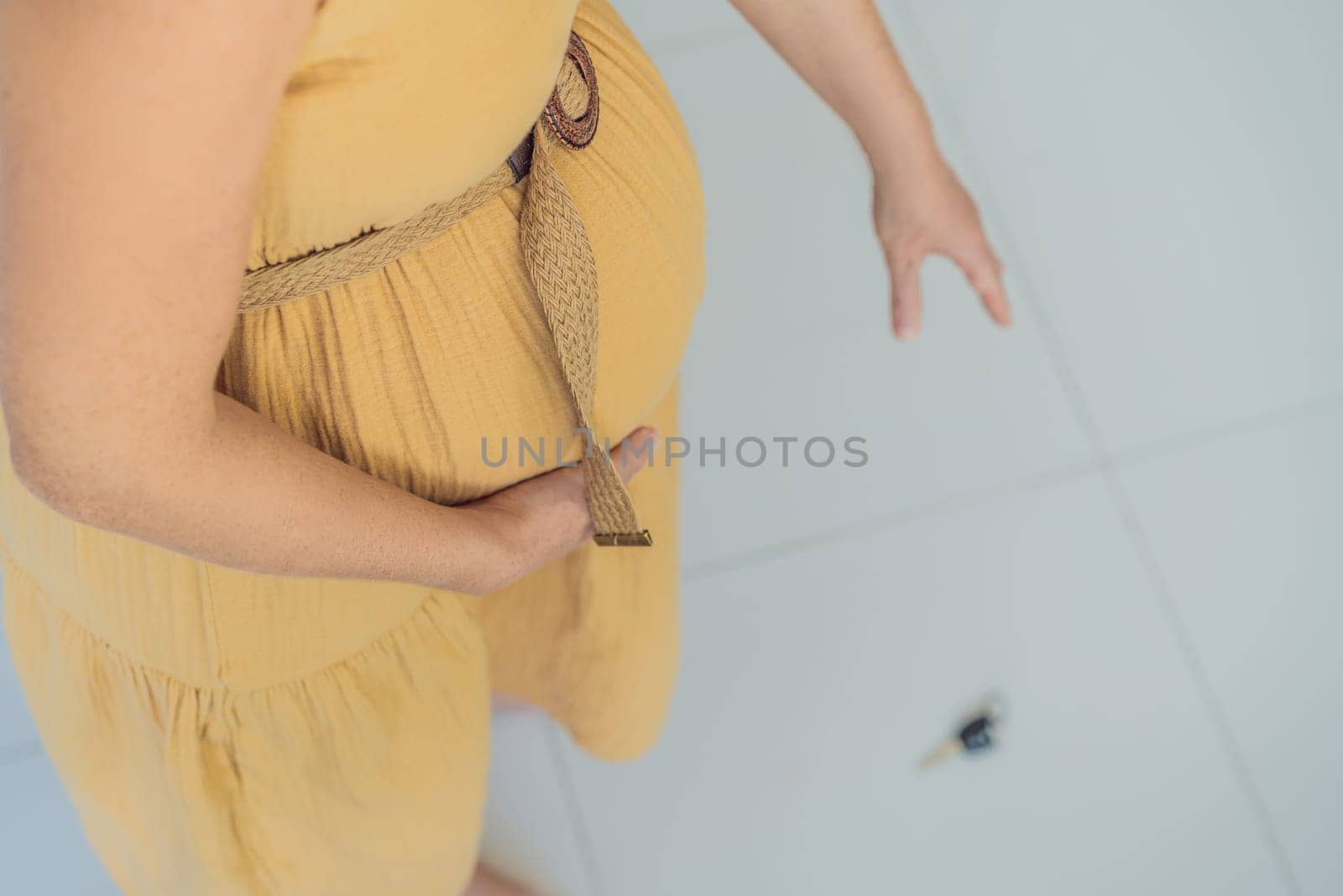 Facing a momentary challenge, a pregnant woman drops her keys and struggles to pick them up, highlighting the physical limitations that can arise during pregnancy. Patience and support become essential by galitskaya