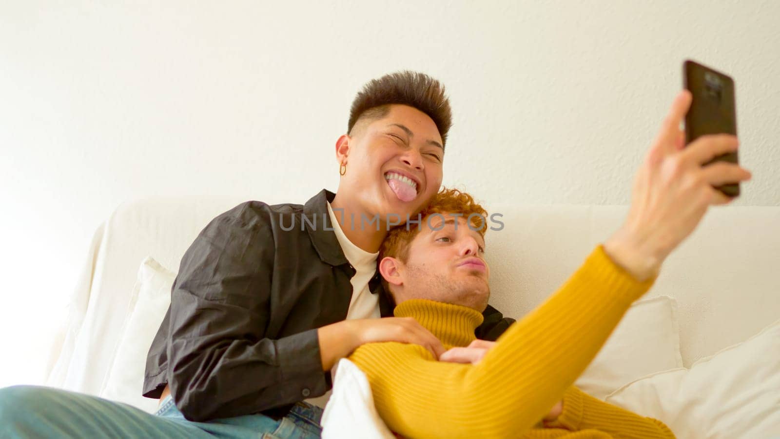 Tender gay couple taking a selfie lying on the sofa at home